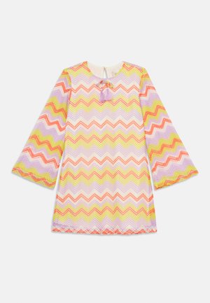 Jaskrawo kolorowa sukienka w zygzakowy wzór w odcieniach różu, żółci i purpury. Posiada długie rękawy oraz okrągły dekolt z zapięciem na sznurek.