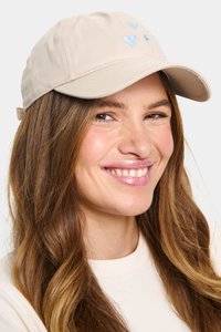 Bézs színű sapka ívelt karimával, az elején három világoskék szív alak hímzett. Puha anyagból készült, hátul állítható pánttal.