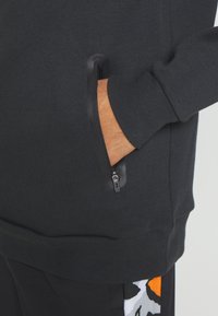 Sweat-shirt noir avec une poche zippée agrémentée d'accents en caoutchouc, des poignets côtelés et une finition texturée.