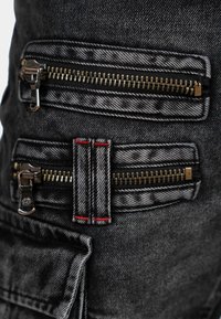 Black denim fabric featuring multiple zippers, showcasing a textured pattern with contrasting red stitching accents. Functional and structured design.