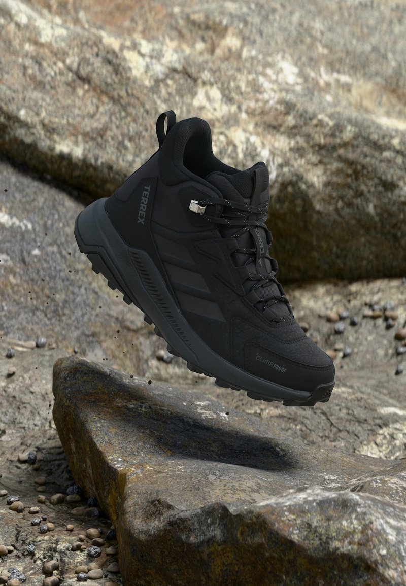 Μαύρο ορειβατικό παπούτσι Adidas Terrex αιωρούμενο πάνω από βραχώδες έδαφος, με σχέδιο κορδονιών και ανθεκτική σόλα για πρόσφυση σε εξωτερικούς χώρους.