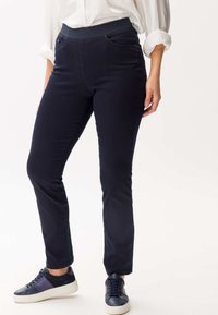 Pantaloni elasticizzati blu navy con un design aderente, vita elastica, tasche frontali e una texture liscia. Abbinati a sneakers scure.