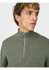 Zielony sweter z dzianiny z wysokim kołnierzem i półzamkiem. Wzór o fakturze, lekki materiał oraz delikatne prążkowanie wzdłuż kołnierza i mankietów.