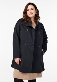 Cappotto nero doppiopetto con ampio colletto, grandi bottoni e una vestibilità rilassata. Presenta una texture liscia e un design che arriva fino al ginocchio.