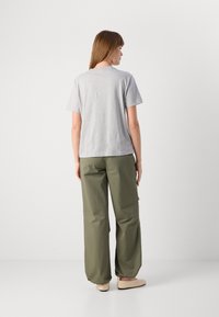 Camiseta gris de manga corta, pantalones holgados verde oliva con puños elásticos y zapatos planos de color claro, vistos desde atrás.