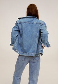 Veste en jean bleu clair avec un col classique, fermeture à boutons et coupe décontractée. Présente des détails usés et des manches à revers.