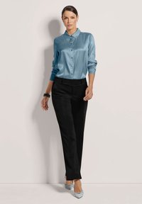 Lichtblauw satijnen blouse met een kraag en knopen aan de voorkant, gecombineerd met zwarte op maat gemaakte broek en lichtblauwe platte schoenen.