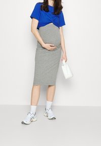 Šedé midi šaty s přiléhavým střihem, kombinované s modrým kratším topem. Bílá kabelka a sportovní boty dotvářejí celý outfit.