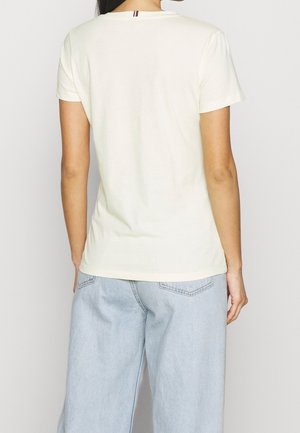 Kremfarvet T-shirt med korte ærmer og rund hals, med en lille rød, hvid og blå detalje på bagsiden, kombineret med lyseblå jeans med vide ben.