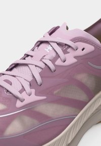 Κοντινή λήψη ενός ροζ και μοβ αθλητικού παπουτσιού με πλέγμα πάνελ, υφασμάτινα κορδόνια και υφή στο μπεζ πέλμα.