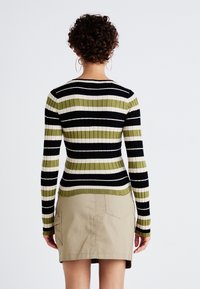 Gestreepte gebreide top in groen, zwart en wit met ribbeltextuur, gecombineerd met een beige rok met zakken en een kort ontwerp.