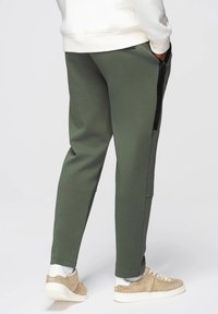 Zielone dresowe spodnie z bawełny z bocznymi kieszeniami i czarnymi zamkami, o zwężającym się kroju nogawki i ściągaczach, w połączeniu z beżowymi sneakersami.