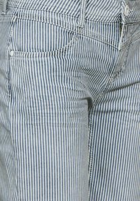 Raidalliset farkut, joissa on siniset ja valkoiset pystyrivat, viisi taskua, nappisuljenta ja ommellut yksityiskohdat.