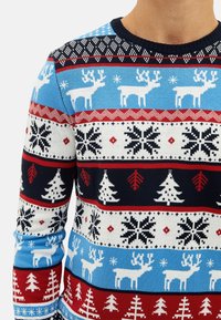 Pull avec un motif festif de rennes blancs, de flocons de neige et de sapins dans des couleurs bleu, rouge, blanc et noir.