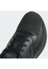 Czarny but sportowy z teksturowaną siateczkową cholewką, plastikowymi akcentami i płaskimi sznurowadłami, o aerodynamicznym kształcie zapewniającym wydajność i wygodę.