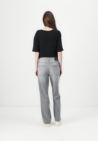 Zwarte katoenen t-shirt met korte mouwen, gecombineerd met losse grijze denim jeans met twee achterzakken en een merklabel.