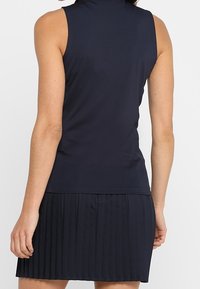 Abito senza maniche di colore blu navy con colletto alto, corpino aderente e gonna plissettata. Realizzato in un tessuto leggero e liscio dal texture uniforme.