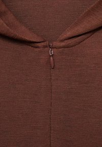 Smeđi teksturirani materijal s kratkim patentnim zatvaračem na izrezu. Čini se da je materijal tkan, s blagim uzorkom.