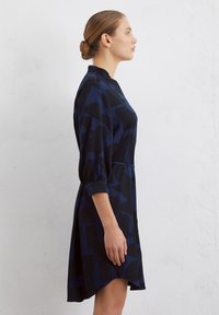 Robe bleu foncé avec un motif géométrique, dotée d'un col haut, de manches trois-quarts et d'un ourlet effilé. Texture de tissu lisse.