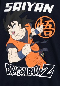 T-shirt nero con un personaggio vestito di arancione e capelli a punte, che tiene un pugno chiuso, insieme al testo "DRAGON BALL Z" e a un simbolo circolare.