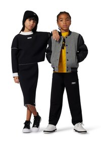 Dos niños visten ropa de DKNY: un suéter negro corto y una falda con detalles blancos, y una chaqueta bomber gris sobre una camiseta amarilla con pantalones negros.