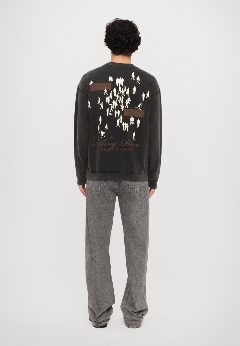 Mørkegrå hettegenser med hvite silhuetter på baksiden, med brune rektangulære detaljer. Kombinert med grå, vide bukser.