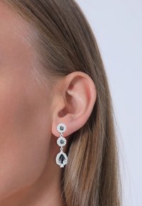 Silverfärgade örhängen med tre svarta ädelstenar i en nivåindelad design, med en päronformad sten längst ner och texturerade detaljer.