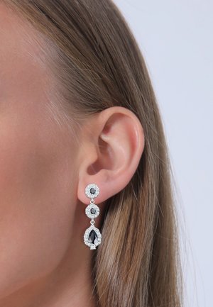 Silberfarbene Ohrringe mit drei schwarzen Edelsteinen in gestufter Anordnung, wobei sich am unteren Ende ein tropfenförmiger Stein und strukturierte Akzente befinden.