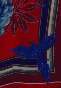 Tissu rouge avec une grande fleur bleue et un oiseau bleu en vol. Le design comprend des bordures contrastées avec des motifs complexes.