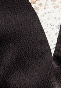 Tela negra con un tejido texturizado, que presenta un inserto triangular de encaje blanco a lo largo de uno de los bordes. El encaje tiene un patrón floral.