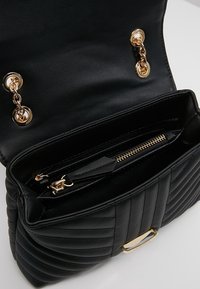 Svart vadderad handväska i syntetläder med guldfärgade detaljer, kedjeaccenser och ett innerfack med dragkedja.