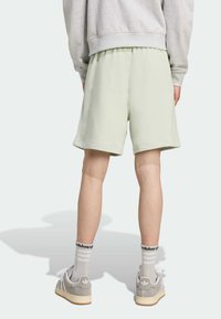 Heledad smaragdrohe puuvillased lühikesed püksid, elastse vöödiga, kantud hallide kingade ja valgete sokkidega, millel on mustad triibud ja logo.