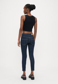 Top corto negro sin mangas combinado con jeans ajustados azul oscuro. Los jeans cuentan con un diseño clásico de cinco bolsillos, costuras visibles y una etiqueta.