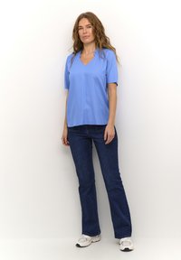 Haut bleu clair à manches courtes avec un col en V, associé à un jean bleu foncé. Le haut présente une texture lisse et une coupe décontractée.