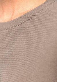 Braun gerippter Strickoberteil mit weitem Rundhalsausschnitt, subtiler Textur und weichem Stoff. Das Detail zeigt die Naht entlang des Halsausschnitts.