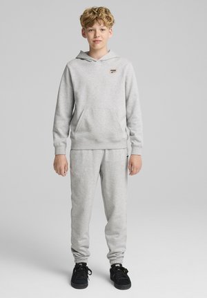 Šedá mikina s kapucí a joggers set vyrobený z měkké látky. Obsahuje klokaní kapsu a logo na hrudi. Spárováno s černými botami.