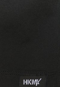 Svart stretchtyg med ribbat mönster; inkluderar en vit logotag som är sydd vid nederkanten. Minimalistisk design utan mönster.