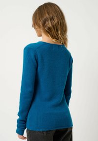 Turkos långärmad tröja i mjukt material med rund halsringning och ribbade ärmslut. Baksidan har en slät, figurnära design.