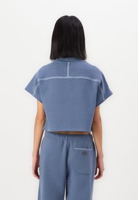 Felpa blu cropped con maniche corte, dettagli di cucitura a contrasto e una vestibilità rilassata, abbinata a pantaloni della tuta blu coordinati.