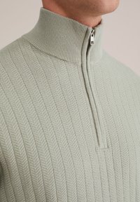 Gai zaļš ribots krekls ar augstu apkakli un pusi rāvējslēdzēja, ar smalku diandru rakstu un mīkstu tekstūru.