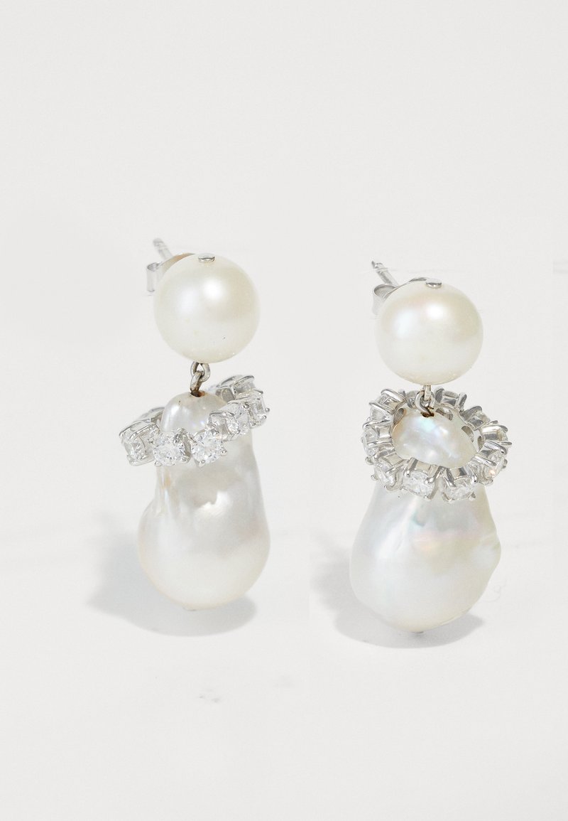 Τα σκουλαρίκια με πέρλες διαθέτουν μια μεγάλη στρογγυλή πέρλα, μια πέρλα με ακανόνιστο σχήμα και λευκά ζιρκόν σε ασημένια βάση με γυαλιστερές φινιρίσματα.