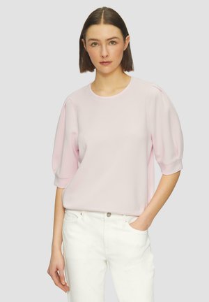 Pullover rosa chiaro con maniche a sbuffo corte. Realizzato in materiale morbido, presenta un collo rotondo e una vestibilità rilassata. Abbinato a jeans bianchi.