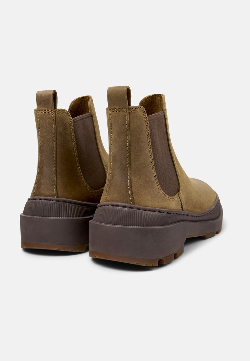 Botas Chelsea de cuero marrón con paneles elásticos en los costados, tiradores y suelas de goma marrón gruesas. Costuras visibles y acentos texturizados.