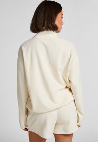 Roomkleurige oversized sweatshirt met een hoge kraag en een zachte textuur, gecombineerd met bijpassende shorts. Eenvoudig, minimalistisch ontwerp zonder patronen.