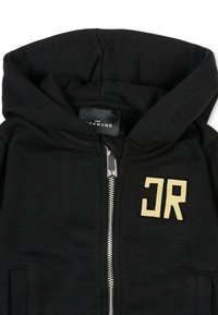 Haut à zip noir avec une texture douce, une capuche doublée et un "JR" jaune contrastant sur le devant. Détails en zip argenté.