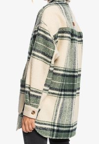 Chaqueta camisa de forro polar en color crema con patrón de cuadros verdes y azul marino. Cuenta con cuello con solapa y puños con botones. Ajuste relajado con bolsillos laterales.