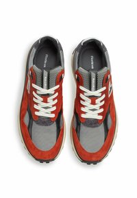 Sneaker in suede rosso e rete grigia con lacci bianchi, dettagli neri e suola con texture. Vista dall'alto che mostra gli occhielli e la linguetta con il marchio.