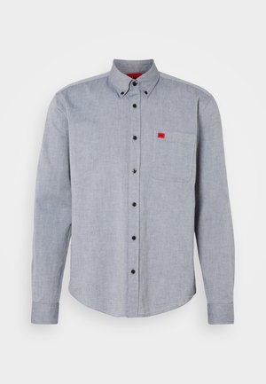 Long-sleeve button-up shirt in light blue fabric, featuring a chest pocket and a red logo patch. Black buttons and a collared neck design.