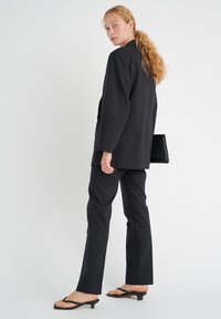 Musta räätälöity bleiseri ja housut, sileä kangas, suora leikkaus, yhdistetty mustiin flip-flop-korkokenkiin ja teksturoituun mustaan käsilaukkuun.