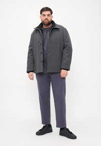 Cămașă din lână gri cu un guler cu fermoar, închidere cu butoane și buzunare laterale. Asortată cu o cămașă de un purpuriu închis și pantaloni tapered, completată de pantofi negri.
